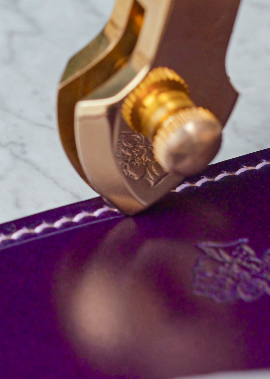 Gold-colored creasing tip setting the border of a Tyrian Heirloom Card Holder, with the Berling logo reflected in the polished tool.